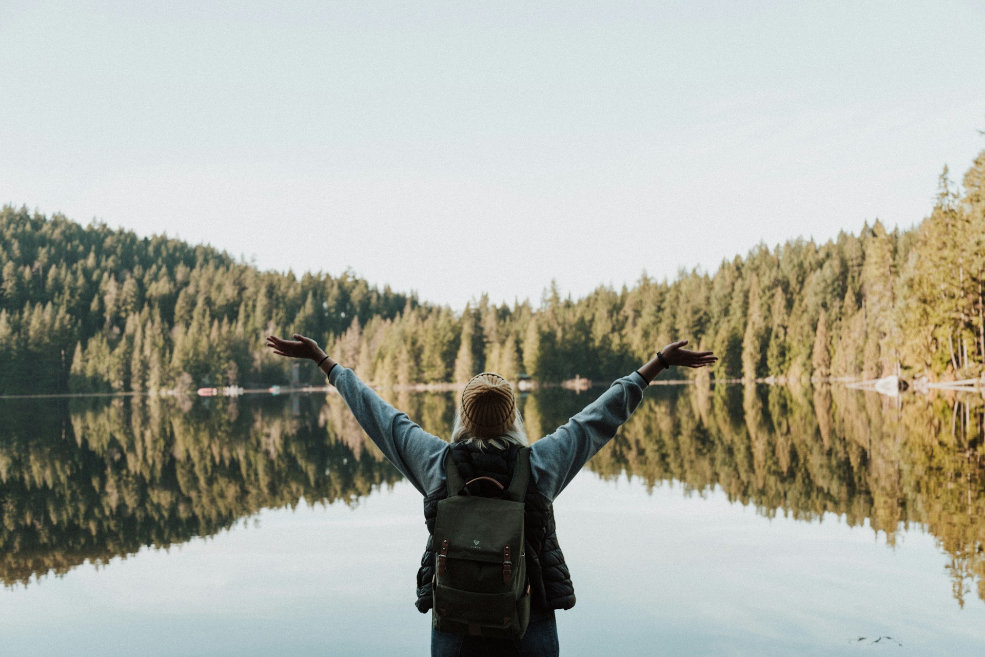 Frau mit ausgebreiteten Armen an einem ruhigen Waldsee – Symbol für Freiheit und Naturverbundenheit